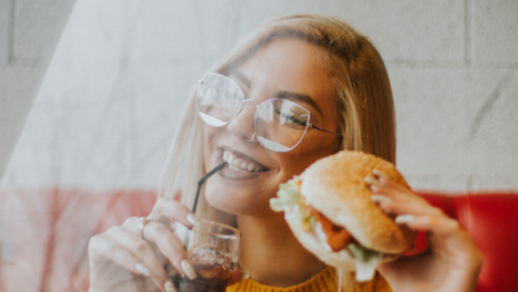 Food trends among college students: A female student enjoys a burger and drink with friends.
