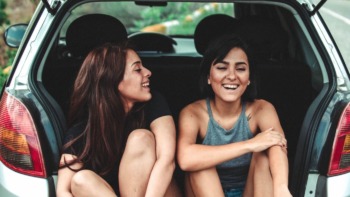 Road-tripping college students sit in the boot of their car.