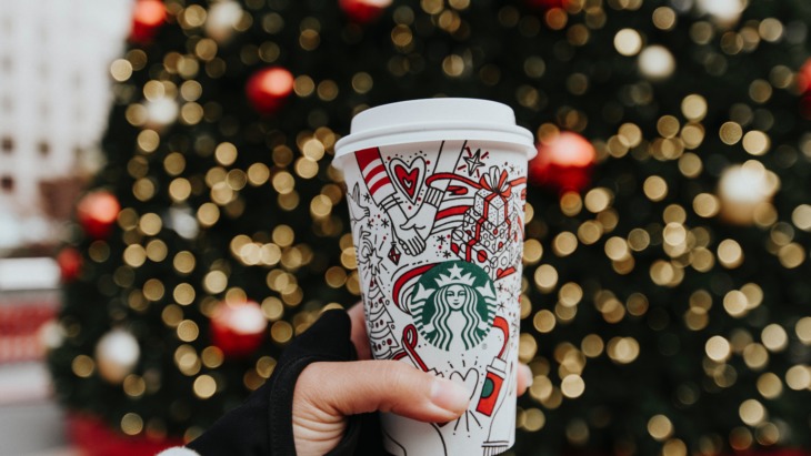 A Starbucks coffee cup in front of a Christmas tree
