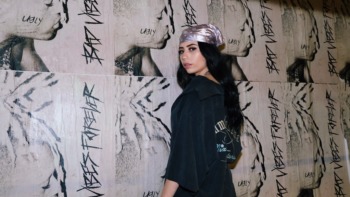 A woman poses in vintage clothing in front of a poster backdrop