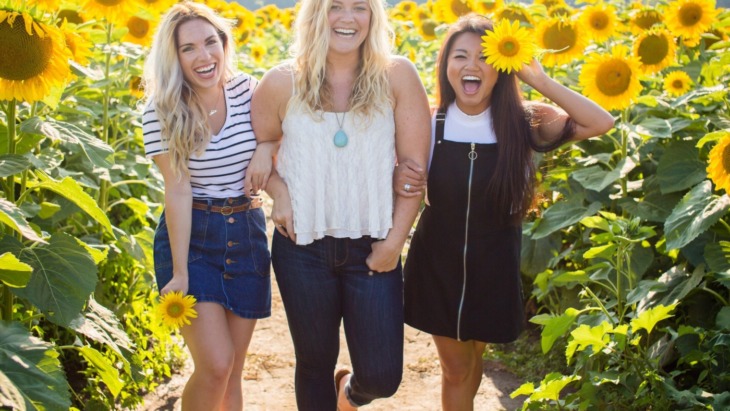 three young women laughing in a scene of sunflowers