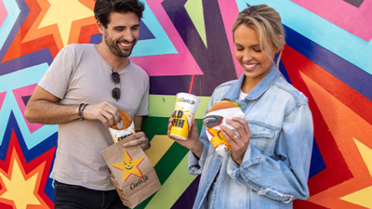 two people stood in front of a colourful wall with Carl Jr food