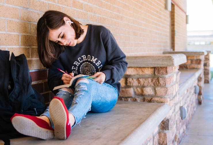 student sat on a bench writing in a book