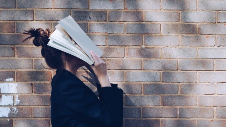 student with an open book covering their face