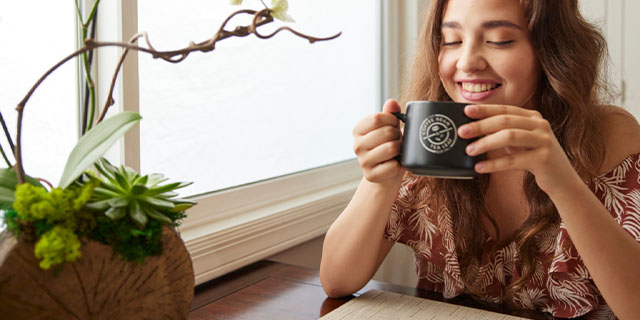 Young person sitting by a window drinking coffee