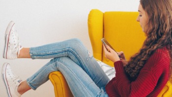 A girl sits on a yellow chair shopping on a phone