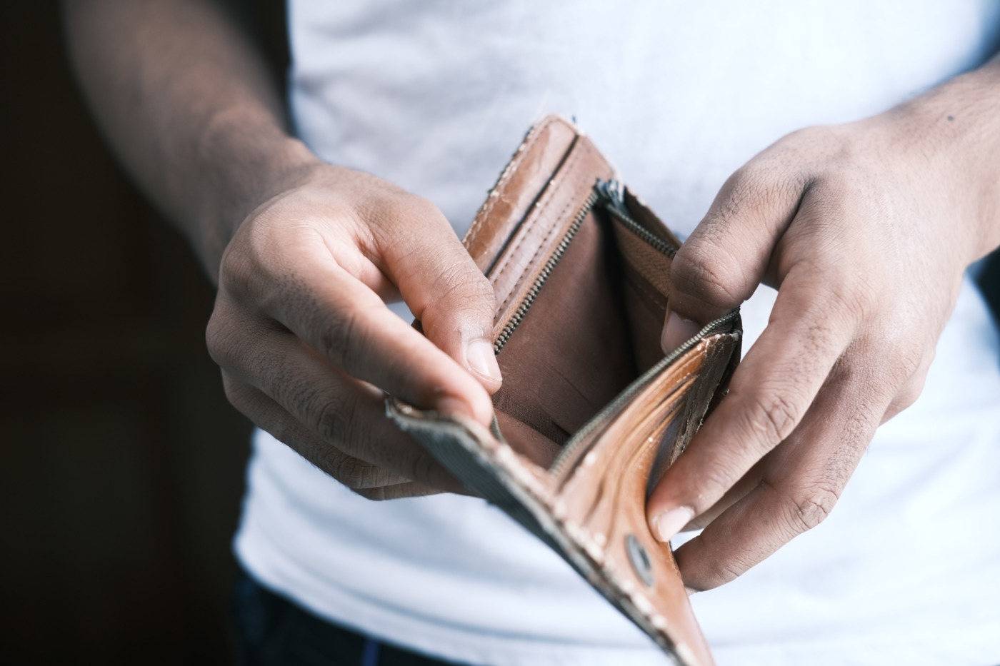 Male student opens empty wallet to illustrate debt