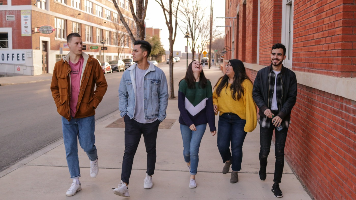 Group of Gen Z friends walking down the street together and laughing. 