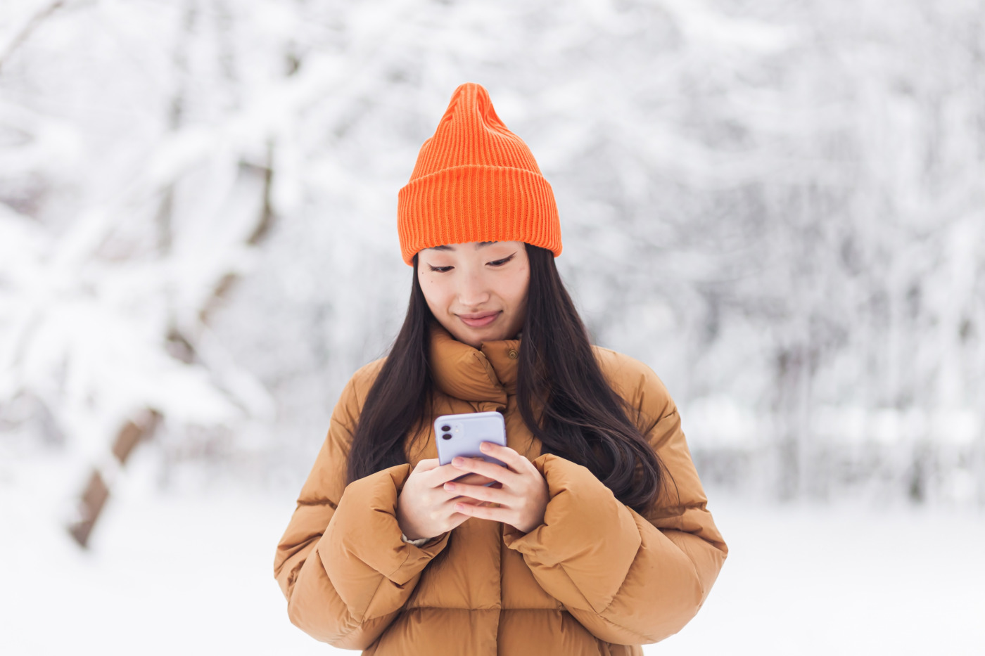Young Gen Z woman walking in the park, uses the phone for online shopping, on a winter snowy day